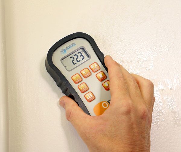 Technician using a moisture meter on drywall to check for hidden water
